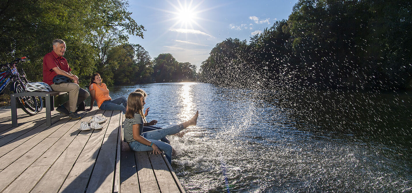 Radfahrende machen Pause am Wasser und plantschen mit den Füßen.