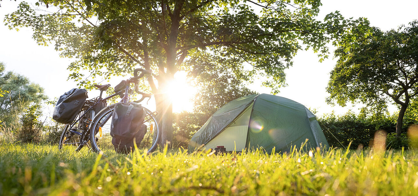 Fahrrad mit Packtaschen und Zelt bei Sonnenuntergang.