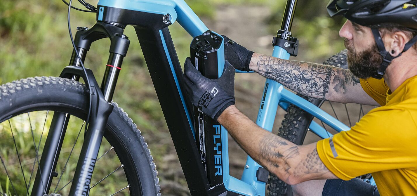 Pedelec-Akku wird entnommen Ein Mann in gelbem Trikot und schwarzem Fahrradhelm entnimmt einen schwarzen Akku aus dem hellblauen Rahmen seines Pedelecs.